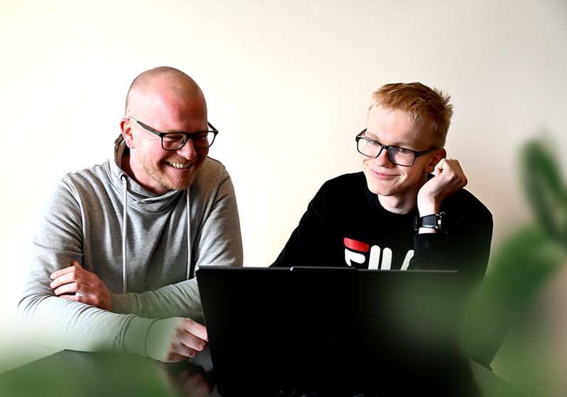 Twee mannen zitten naast elkaar en werken samen achter een computer.
